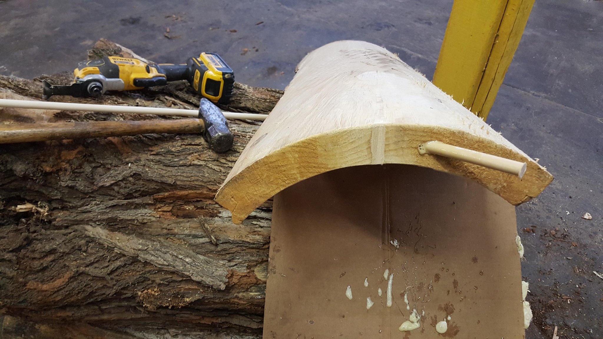 Dowel rod fully seated in the spline channel, DeWalt oscillating tool in background — cardboard backing visible inside the hollow cavity, IC WOOD production shop